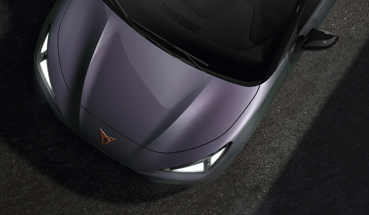 Vogelperspektive auf die Motorhaube des CUPRA Raval in schimmerndem Plasma-Lack mit kupferfarbenem CUPRA-Logo und leuchtenden LED-Scheinwerfern.